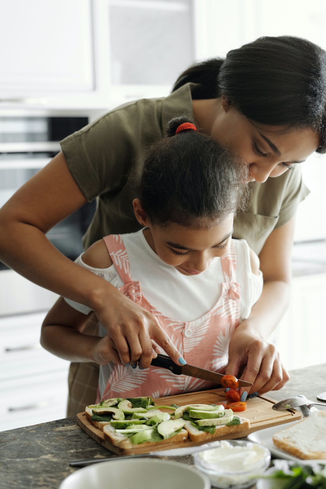 a mother helping her daughter cut vegetables